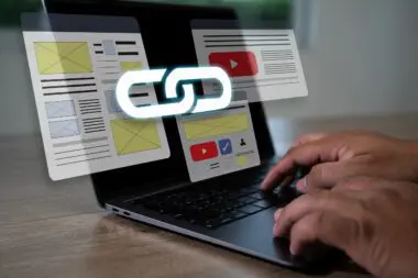 Hands typing on a laptop with glowing link icon floating above wireframe website layouts.