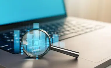 Magnifying glass resting on a laptop keyboard displaying a glowing blue AI circuit board icon.