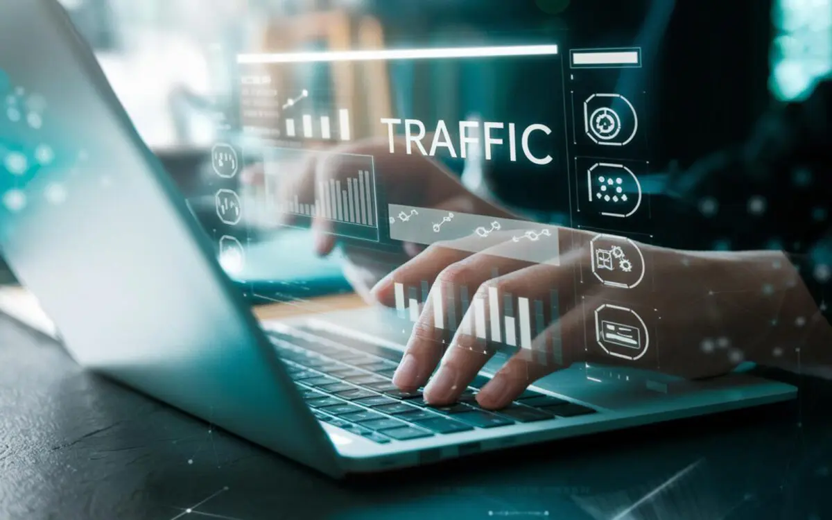 Close-up of hands typing on a laptop with digital overlays showing traffic statistics and analysis icons.