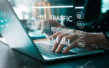 Close-up of hands typing on a laptop with digital overlays showing traffic statistics and analysis icons.