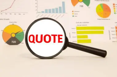 A magnifying glass rests on a surface, highlighting the red word QUOTE against a background of various business data charts.
