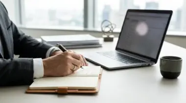 Executive leader writing strategic professional article in notebook, laptop and coffee cup nearby