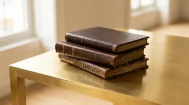 Stack of old leather-bound books on a gold desk, representing the business books that shaped the world's richest people.