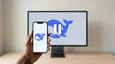 Hand holding smartphone with DeepSeek whale app icon before monitor displaying pause symbol over whale logo, representing funding halt amid AGI race.