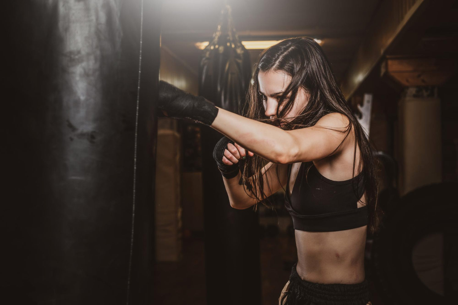 Thinking like Google algorithm - Skinny focused woman has boxing training with punching bag dark gym